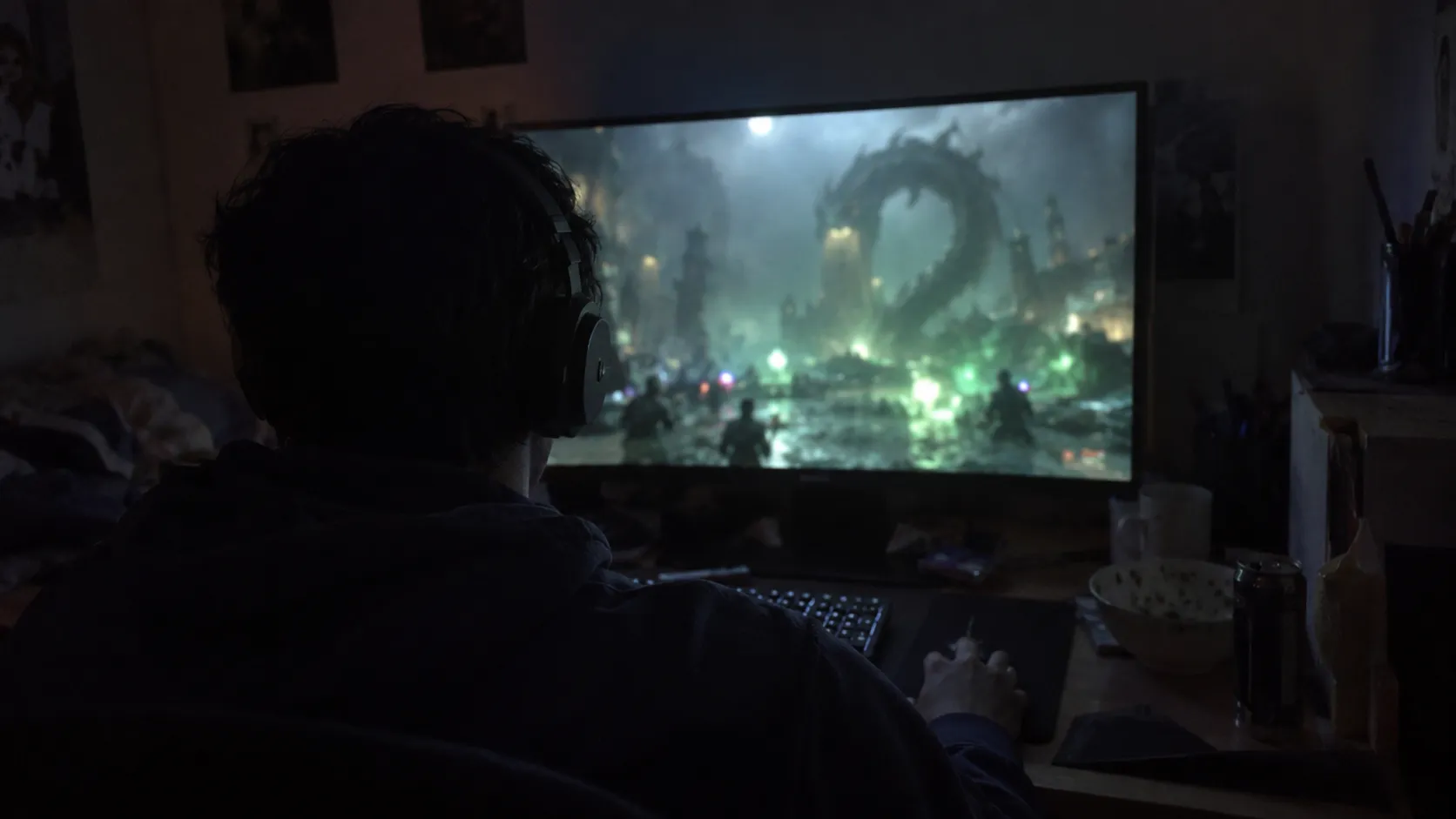 A player in a headset raiding late at night, the monitor glowing green with a blurred boss fight