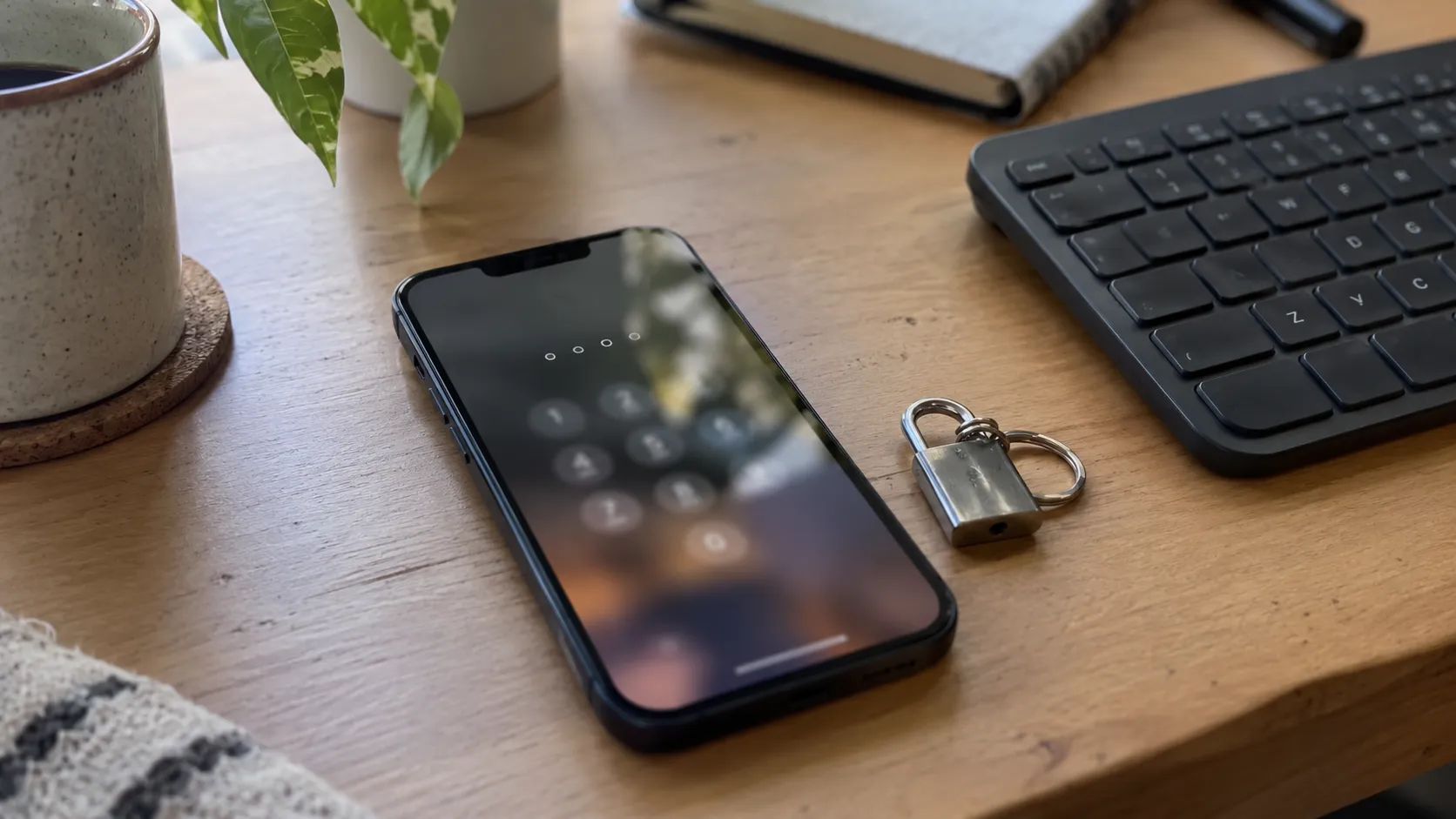 A phone showing a blurred security code screen next to a keyboard and a small padlock keychain